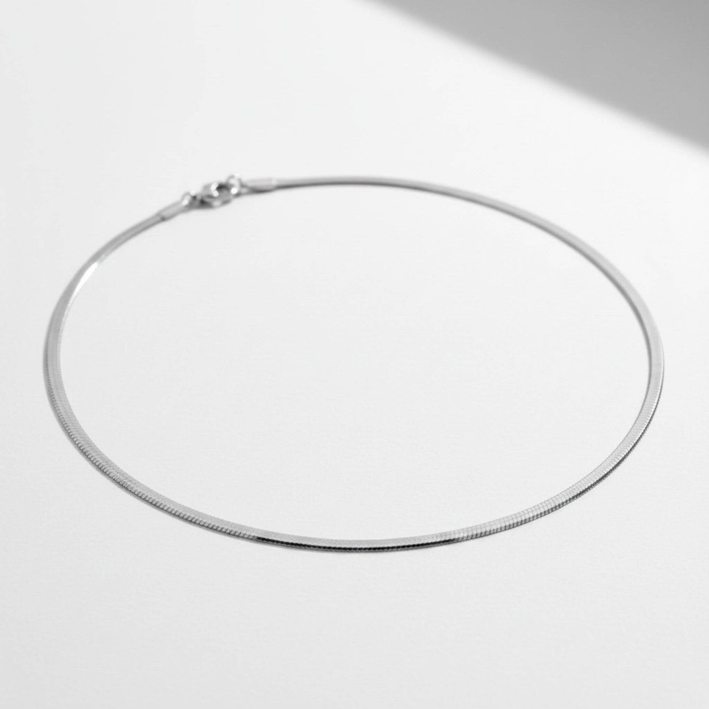 Silver 3mm herringbone necklace laid flat, 18-inch length, lobster claw clasp, hypoallergenic stainless steel