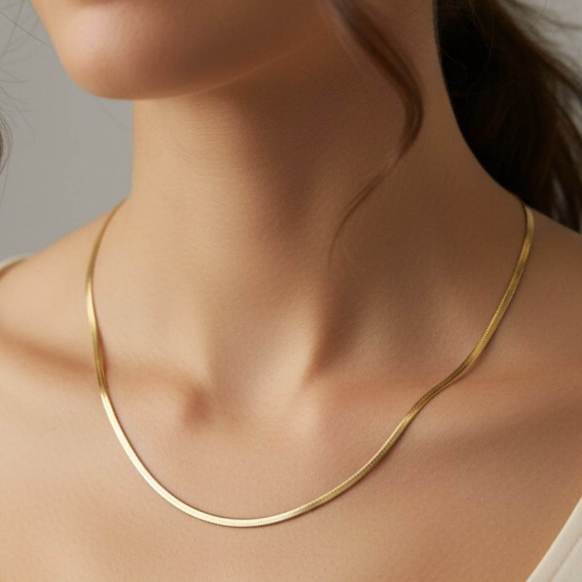 Close-up of 18K gold herringbone chain necklace on model's neck, 3mm wide stainless steel with gold PVD coating