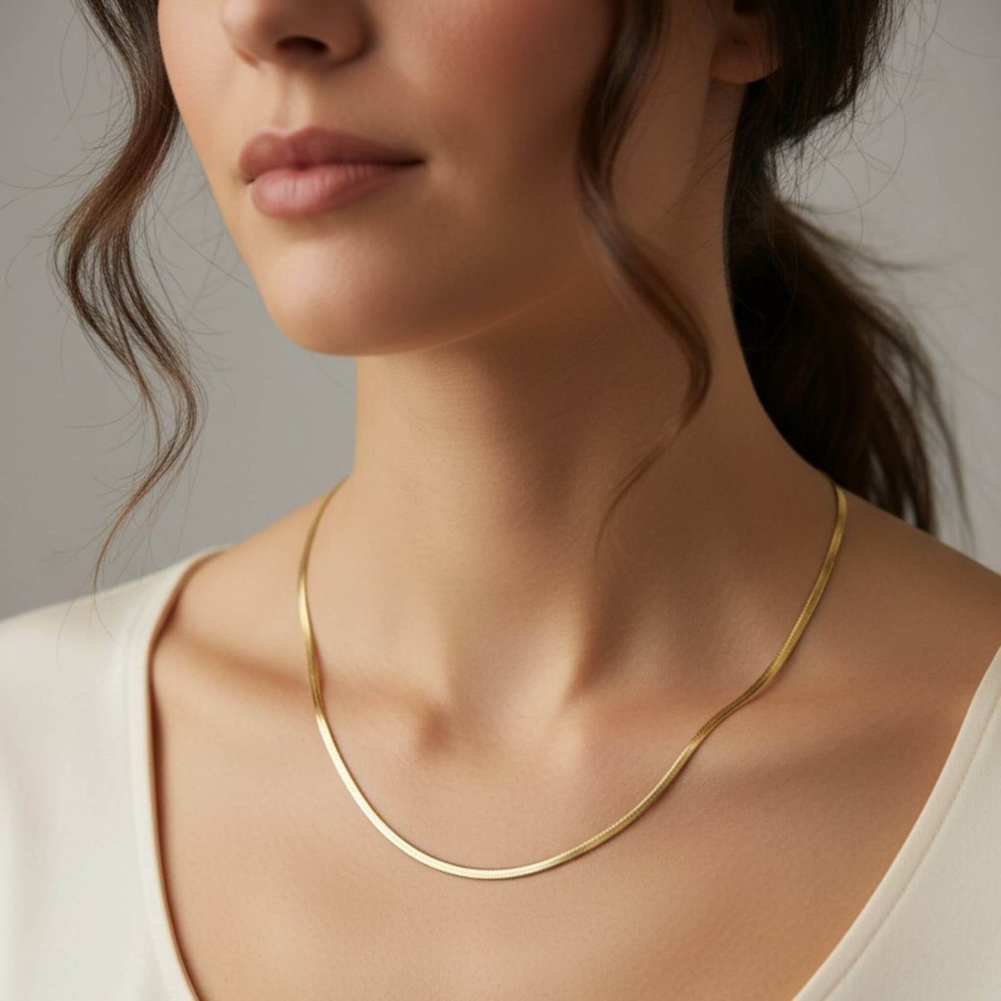 18-inch gold herringbone necklace worn on model, 3mm flat snake chain in 18K gold plating, sitting at the collarbone