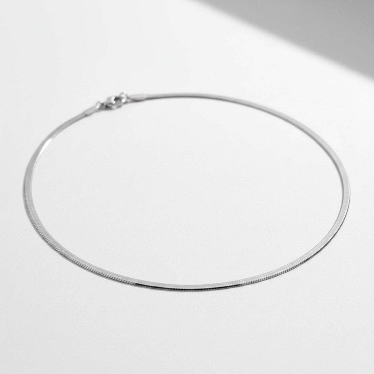Silver 3mm herringbone necklace laid flat, 18-inch length, lobster claw clasp, hypoallergenic stainless steel