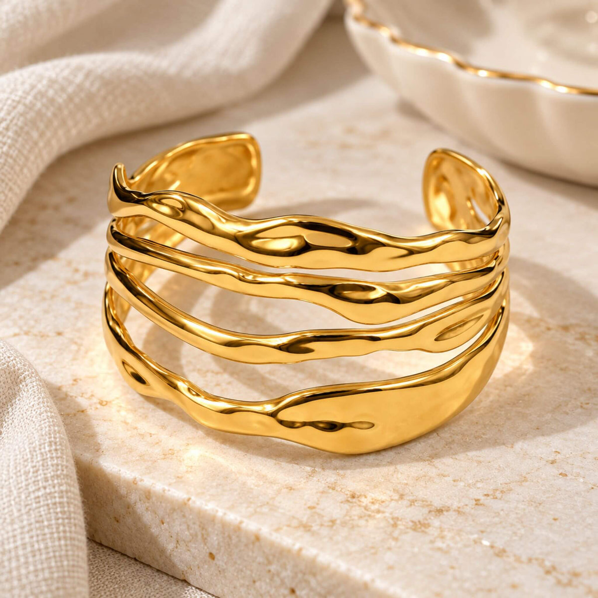 18K gold cuff bracelet with polished multi-band wave design displayed on a neutral stone surface