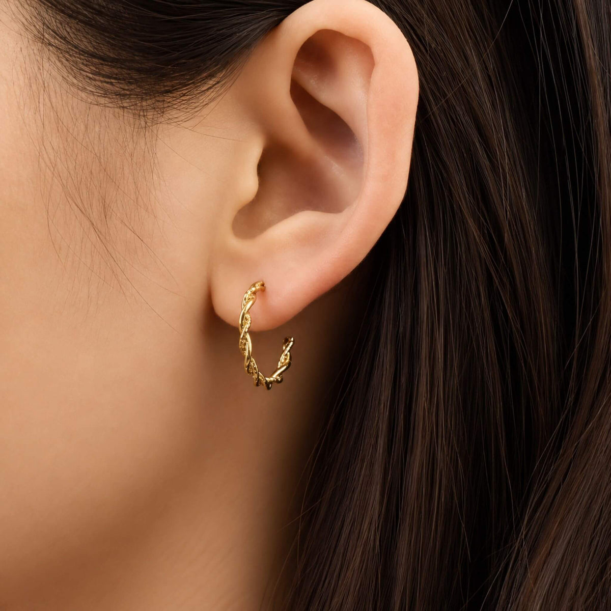 Woman wearing 18K gold plated twisted rope hoop earrings with a textured spiral design.