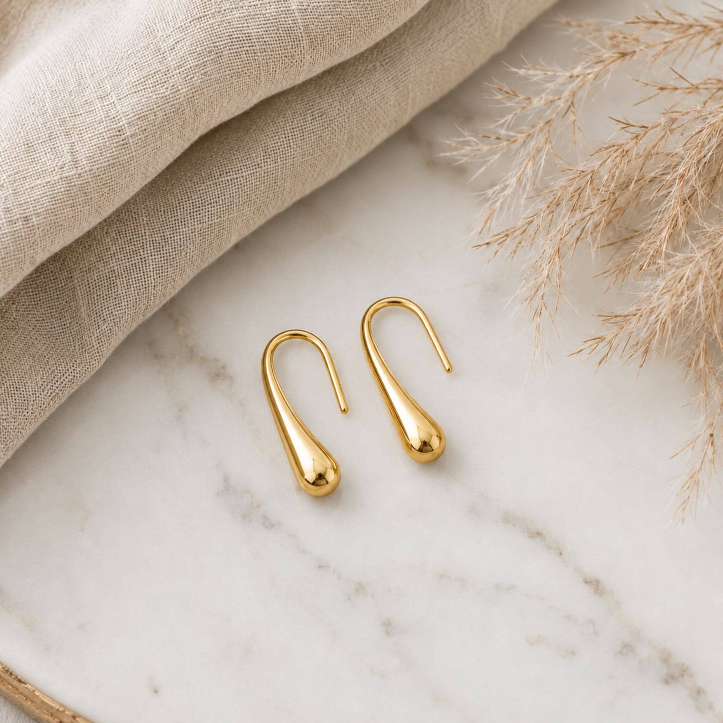 18K gold plated stainless steel teardrop hook earrings displayed on a marble surface with neutral linen fabric, lightweight hypoallergenic earrings for everyday wear.