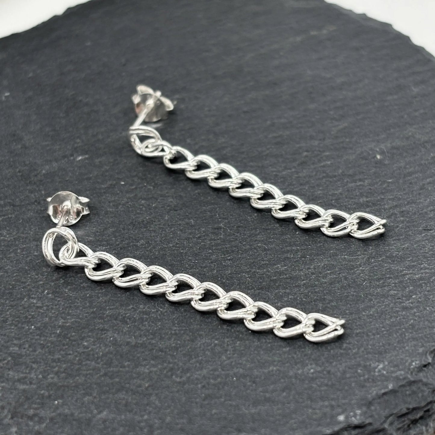 Closeup of dangle stud earrings in polished sterling silver curb chain design