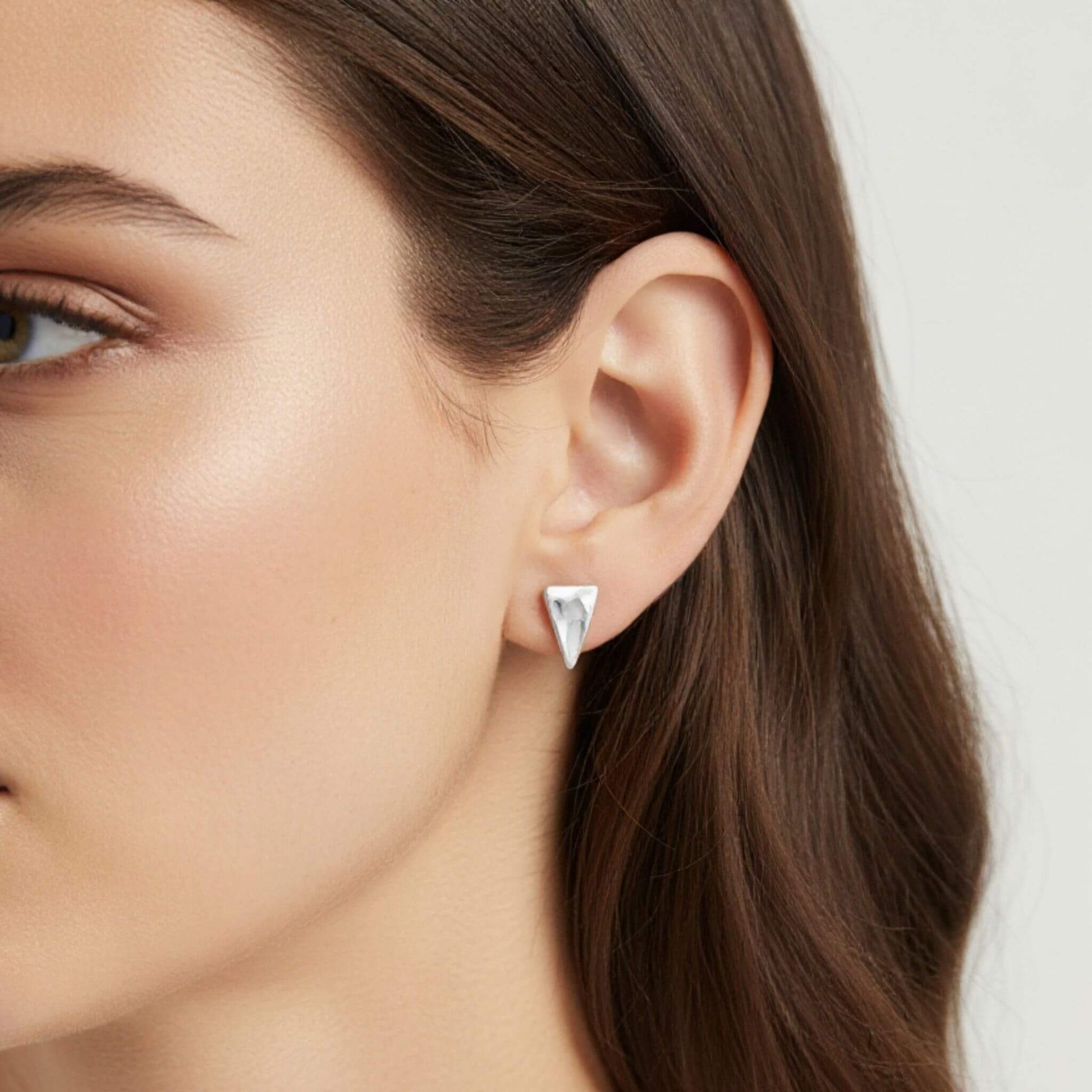 Elongated hammered triangle stud earrings in sterling silver worn on ear, minimalist everyday stud earrings