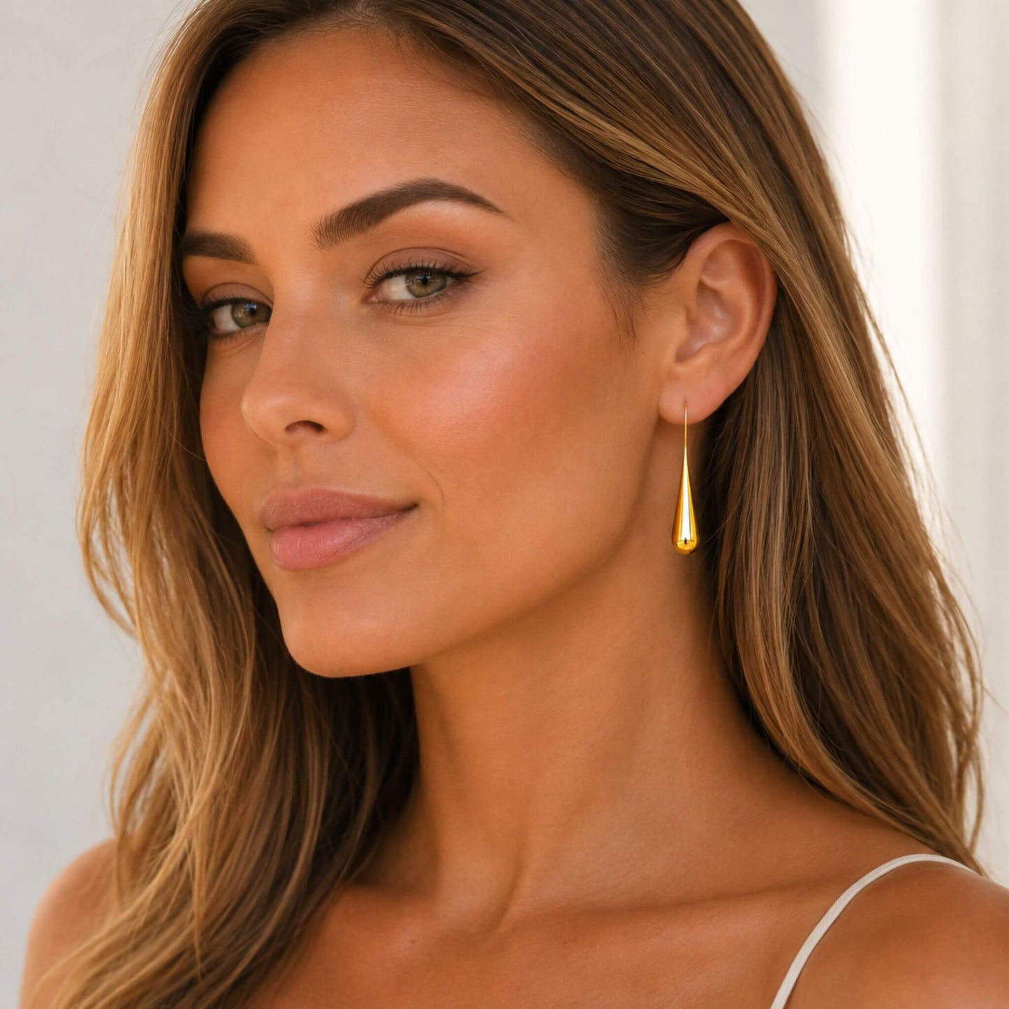 Woman wearing 18K gold plated gold dangle earrings made from hypoallergenic stainless steel with a modern teardrop design.
