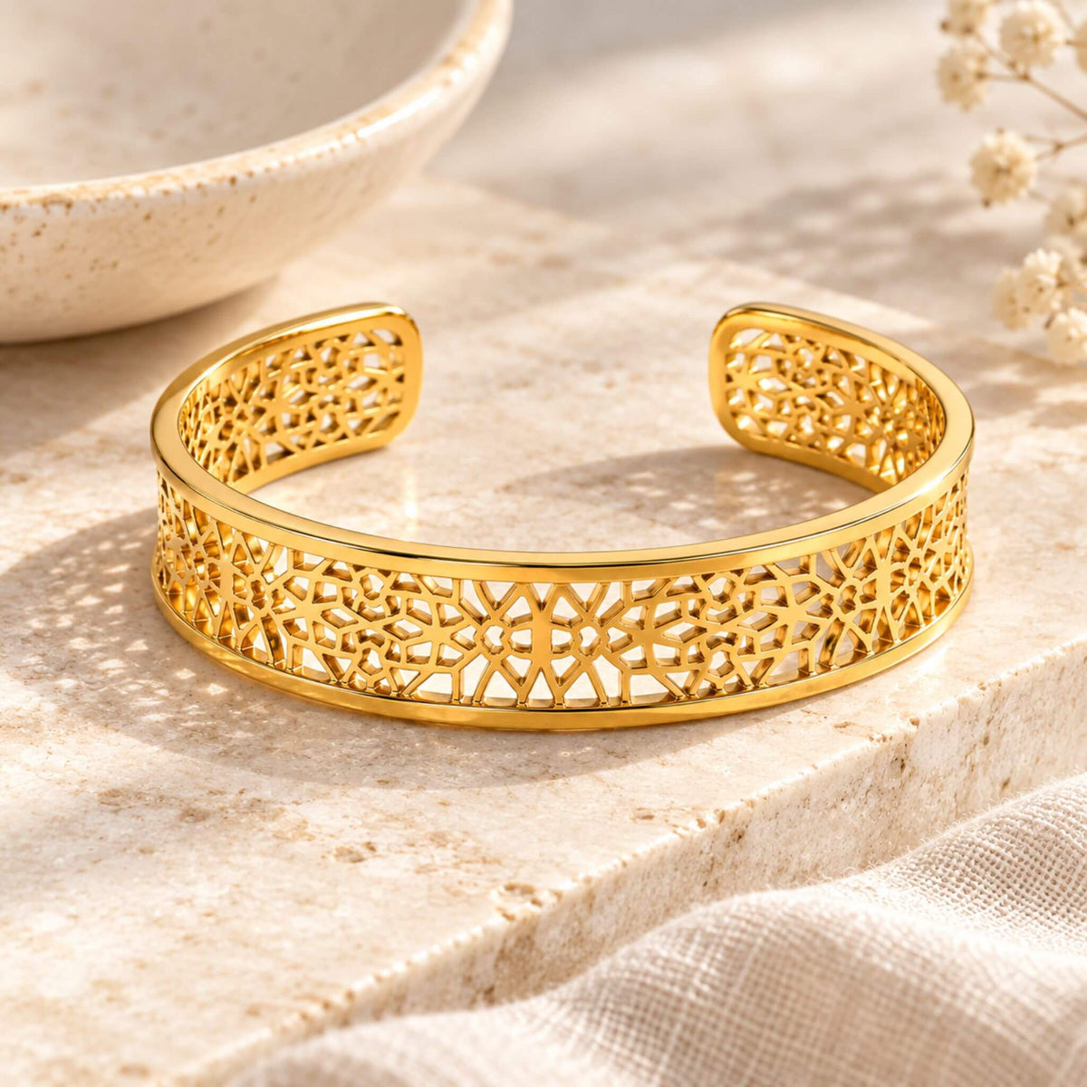 Gold filigree open cuff bracelet for women with intricate openwork design displayed on neutral stone