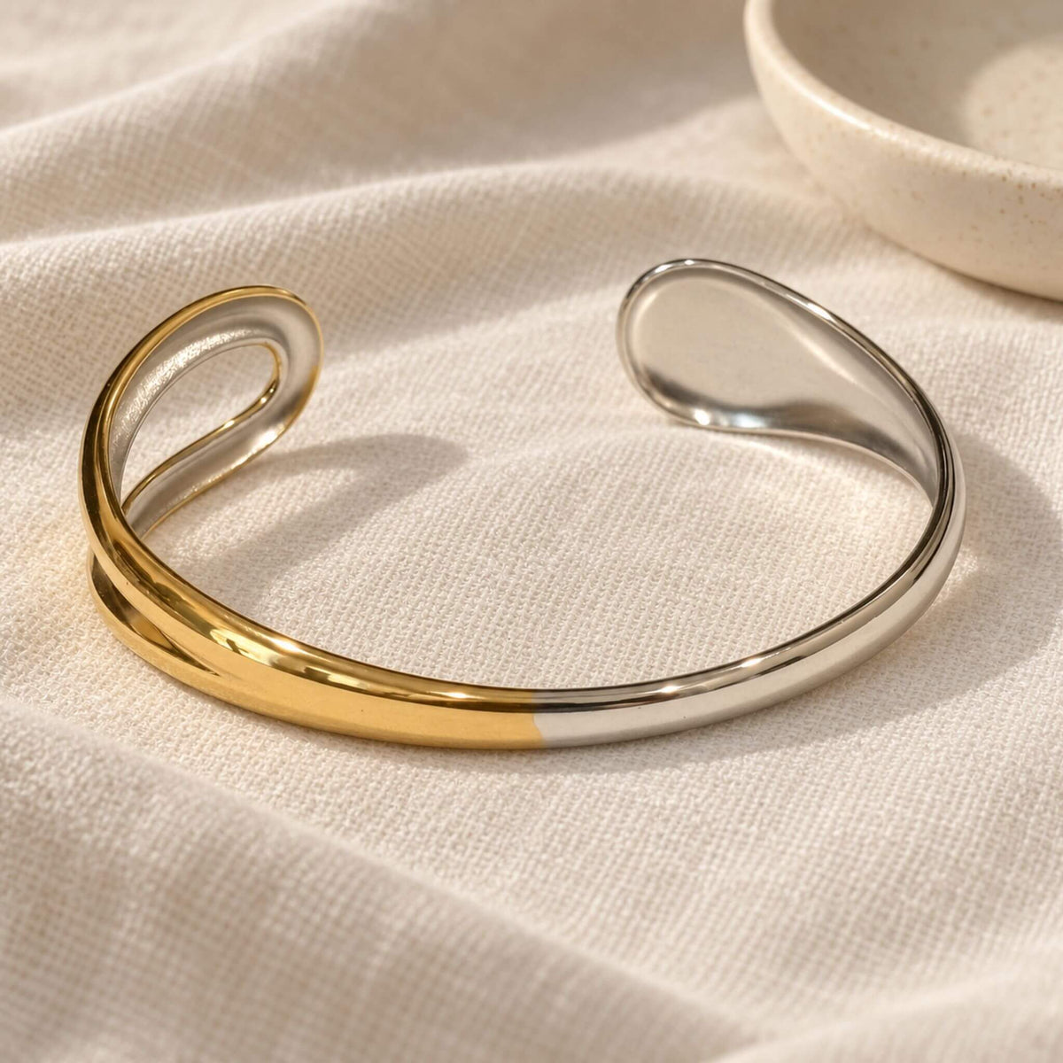 Back view of a gold and silver sculptural cuff bracelet on ivory linen, showing the smooth band and inside surfaces of both ends.