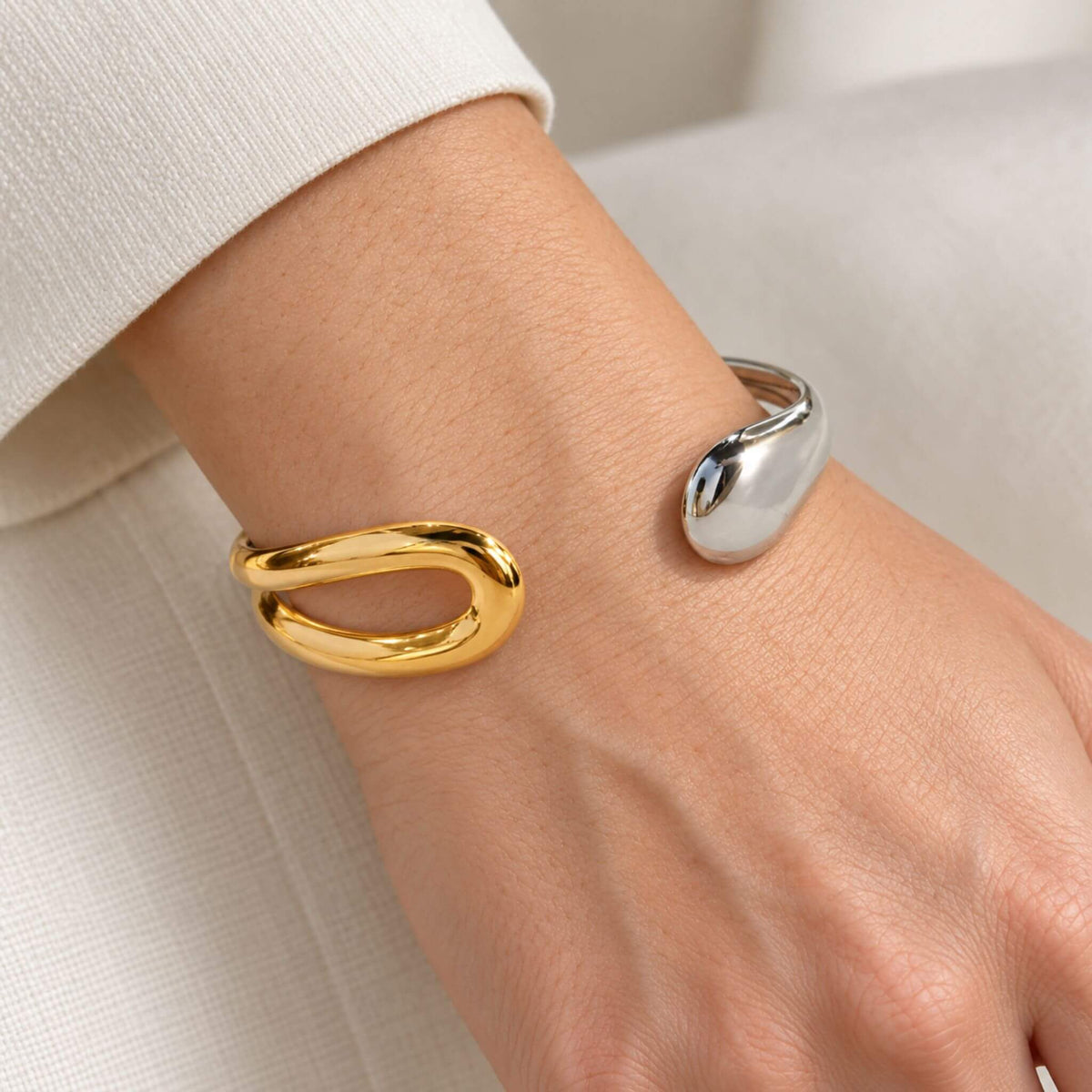 Close-up of a gold and silver sculptural cuff bracelet on a woman's wrist, showing its open design and polished ends.