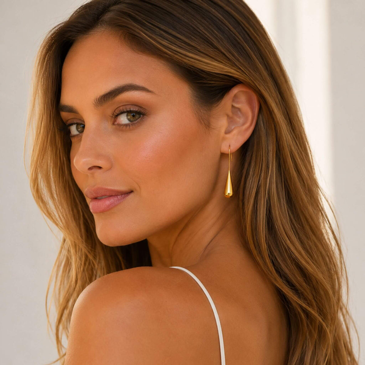 Model looking over her shoulder wearing elegant 18K gold plated gold teardrop earrings made from hypoallergenic stainless steel.