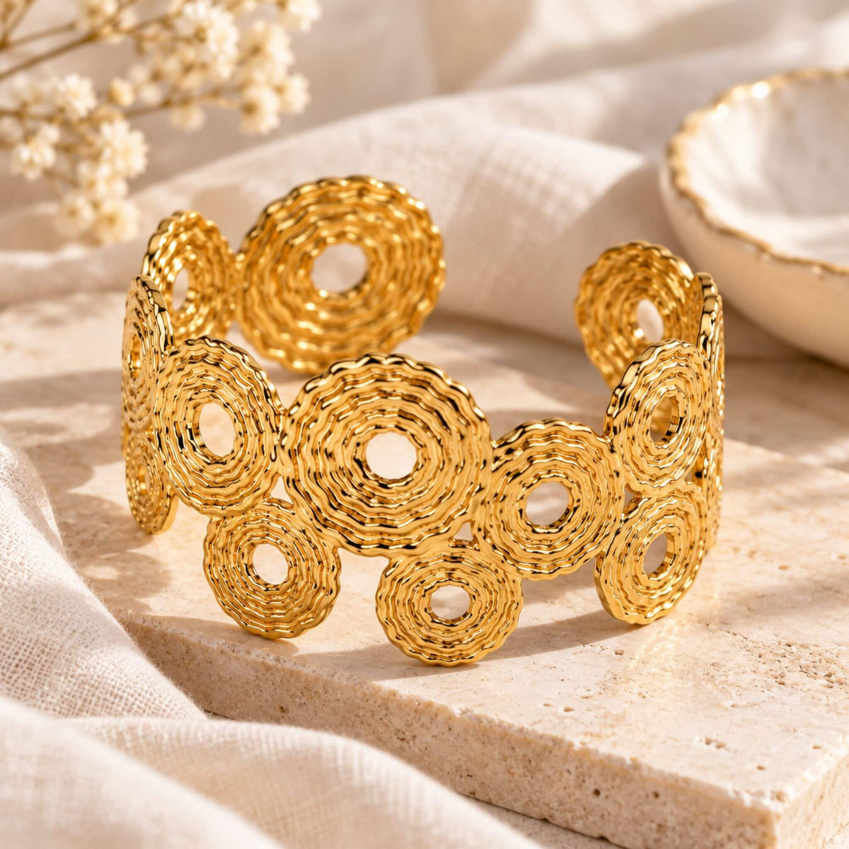 Gold textured circle cuff bracelet displayed on a neutral stone surface