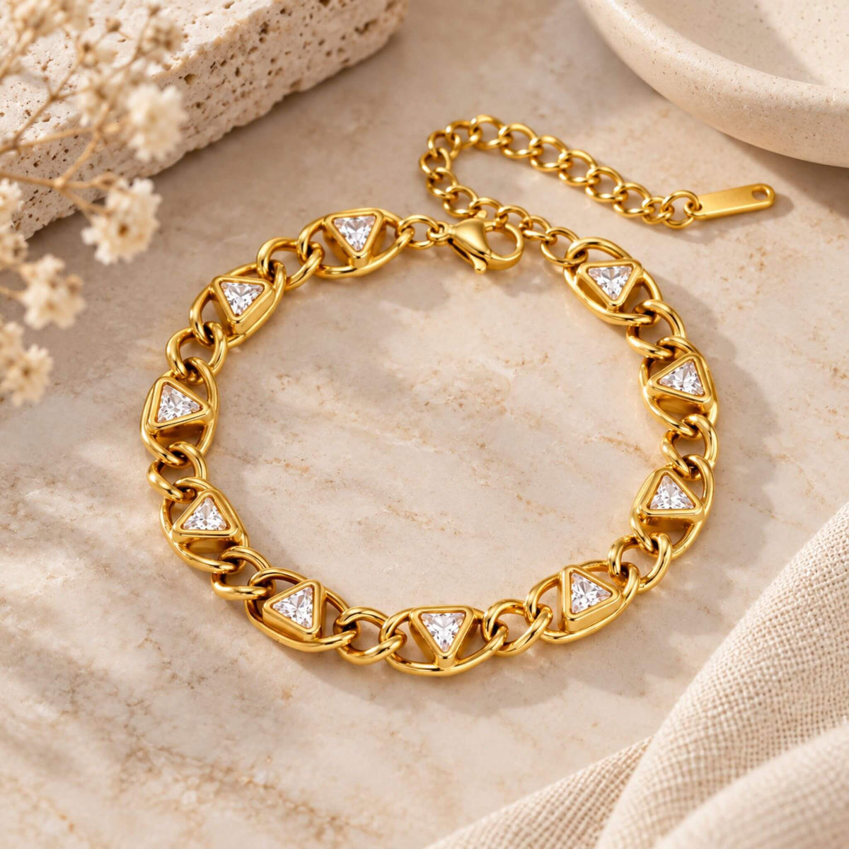 Gold zircon tennis bracelet with triangular white stones and adjustable chain displayed on a neutral flat lay