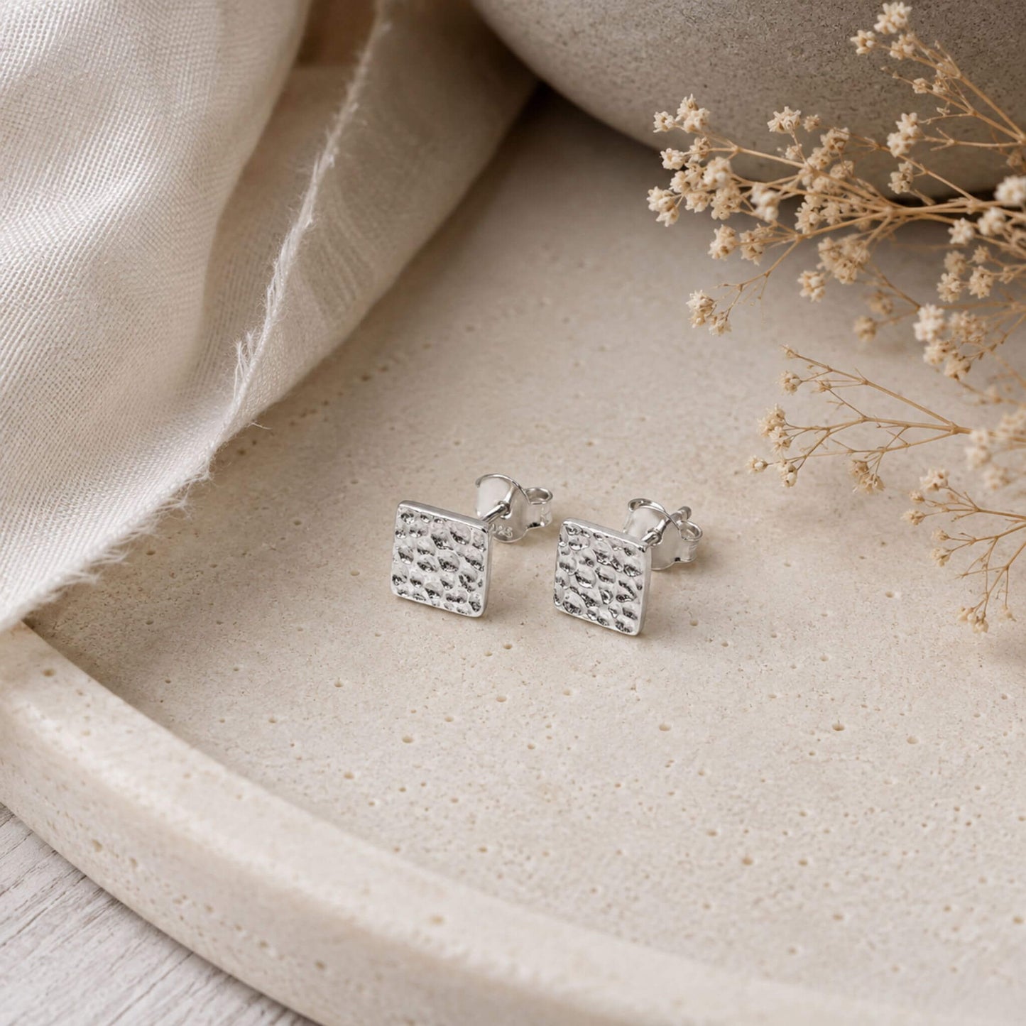 Hammered silver stud earrings in square design styled on neutral jewelry display