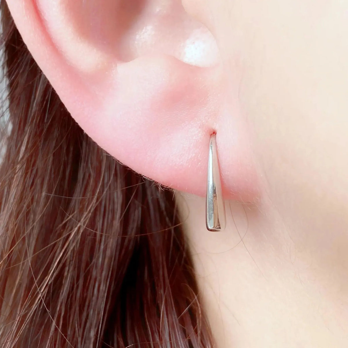 Polished silver stainless steel teardrop hook earrings worn on ear – minimalist hypoallergenic women’s jewelry