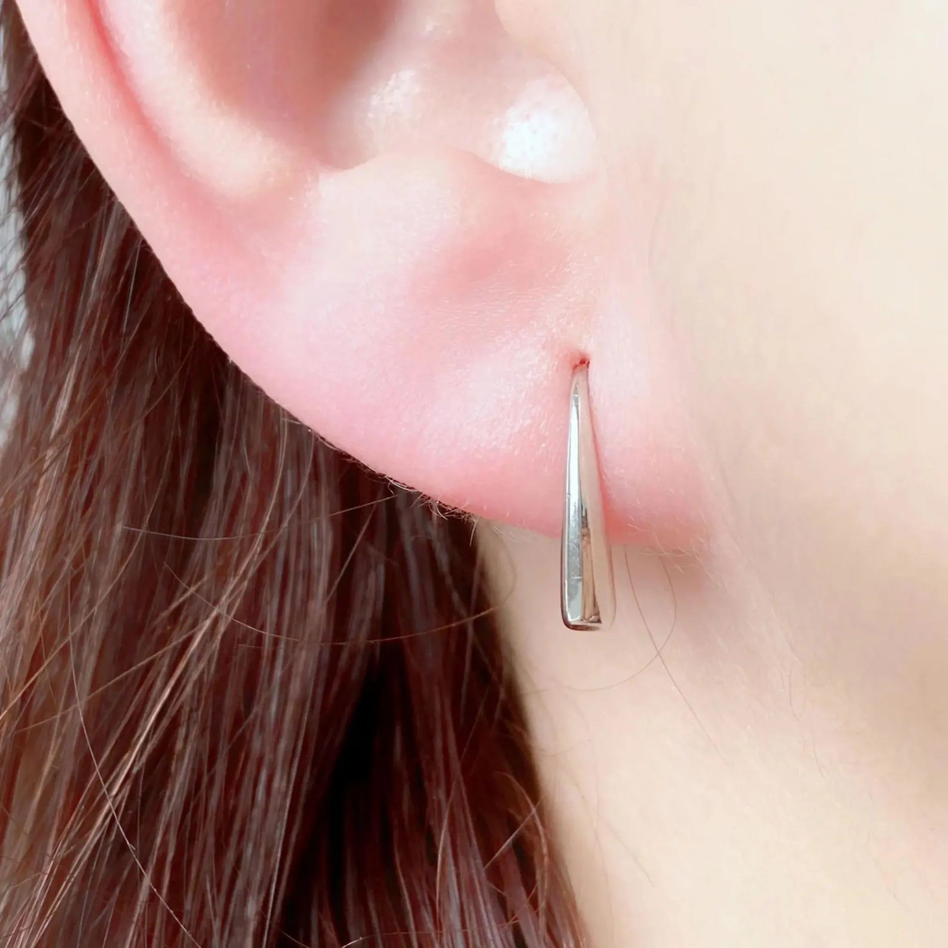Polished silver stainless steel teardrop hook earrings worn on ear – minimalist hypoallergenic women’s jewelry
