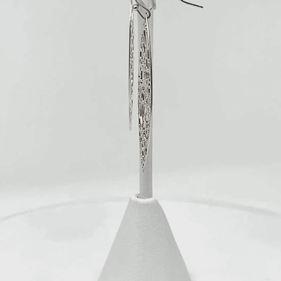 Close-up view of silver teardrop earrings, highlighting the delicate shimmer and random line detail.