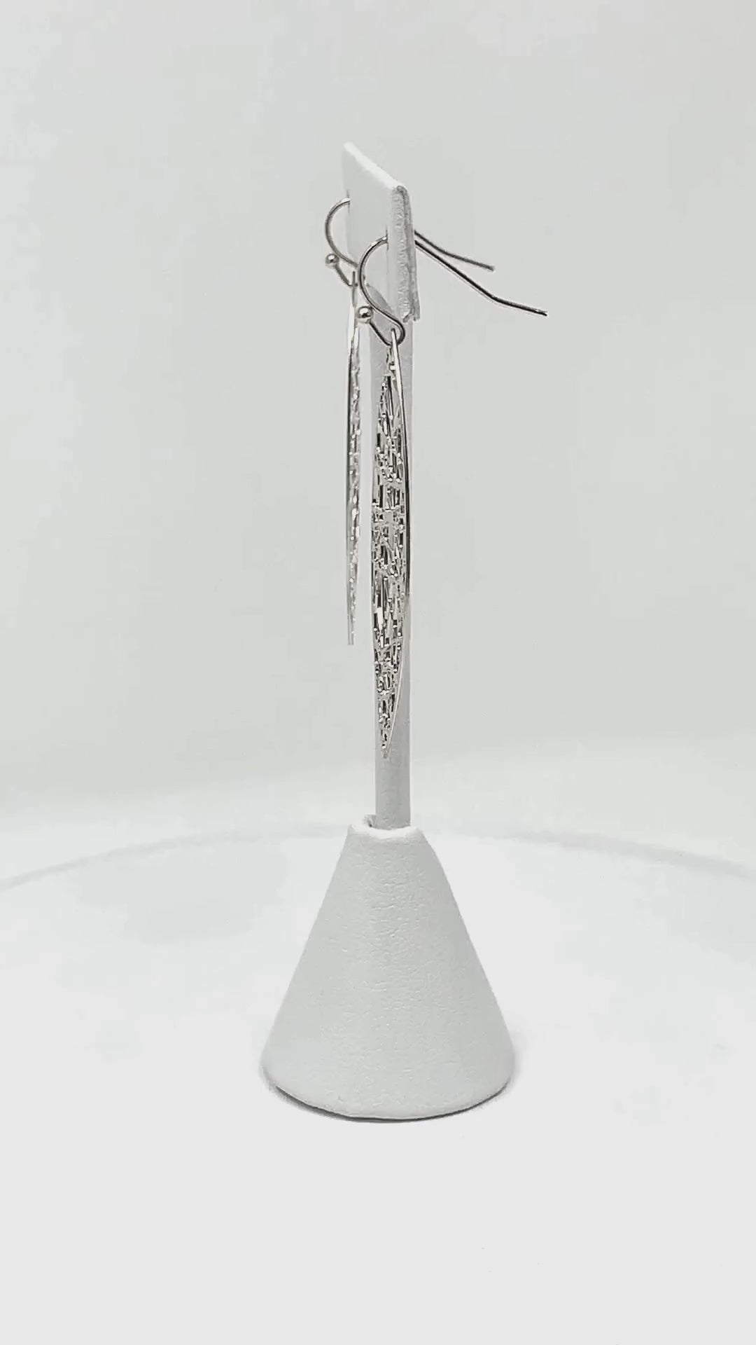 Close-up view of silver teardrop earrings, highlighting the delicate shimmer and random line detail.