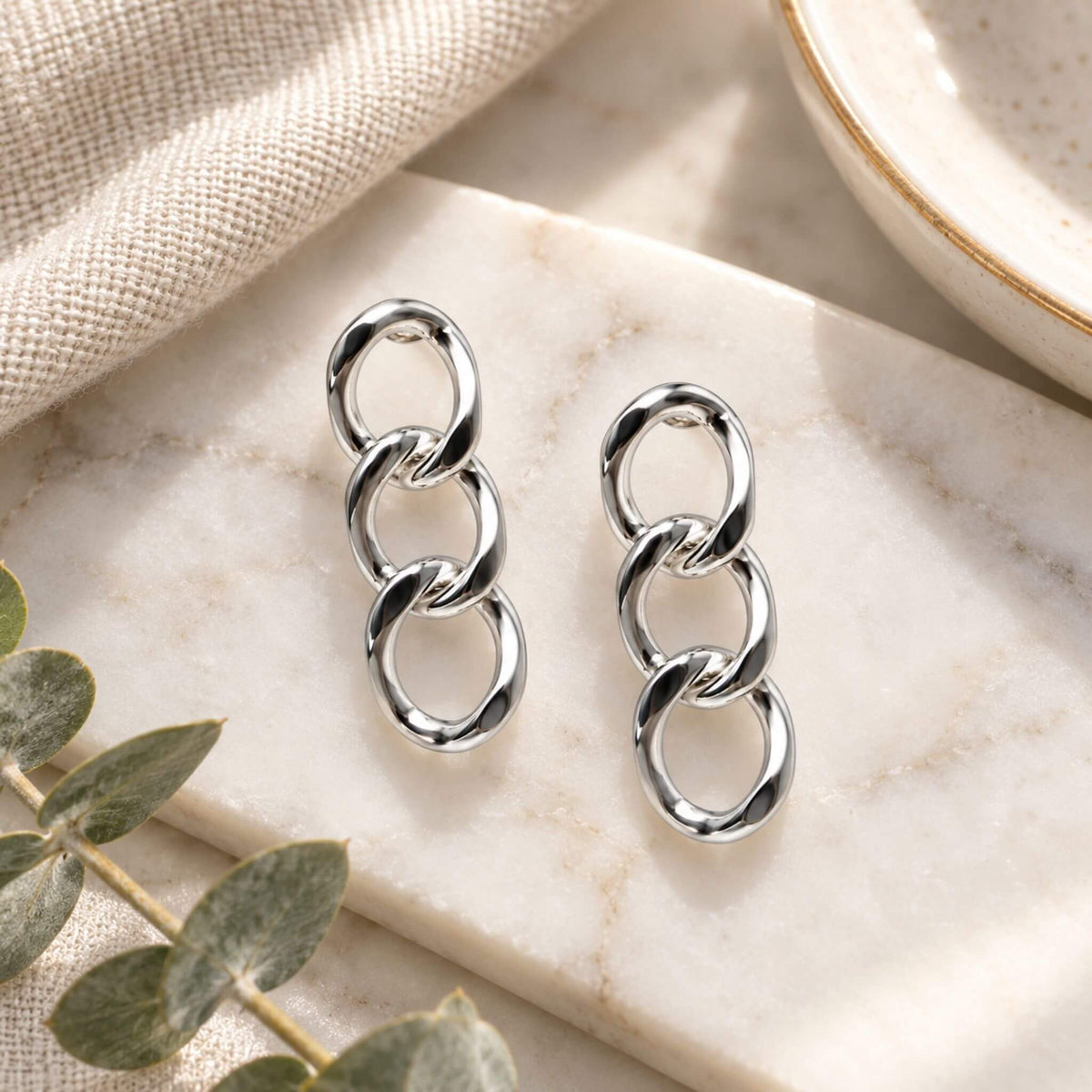 Silver chain earrings with three polished interlocking links on marble