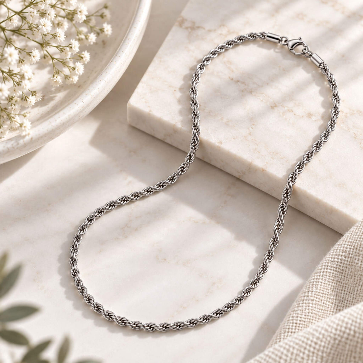 Silver stainless steel rope chain necklace styled on a neutral marble surface