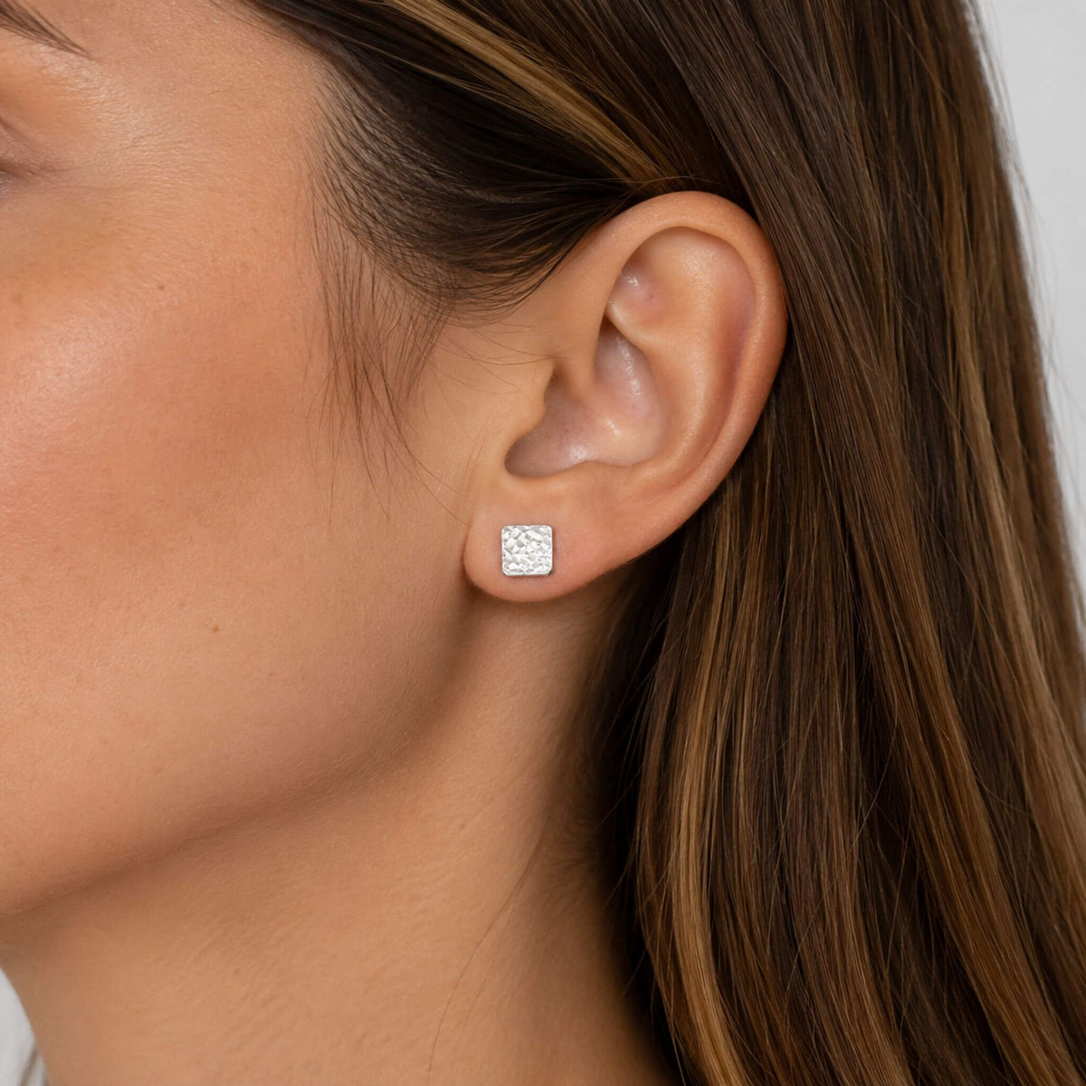 Silver square stud earrings shown on ear with hammered sterling silver finish