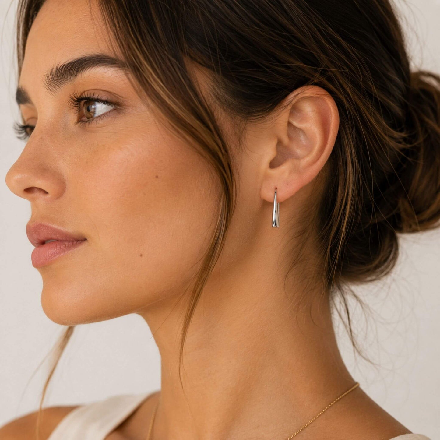 Model wearing polished silver stainless steel teardrop hook earrings in a minimalist side profile view.