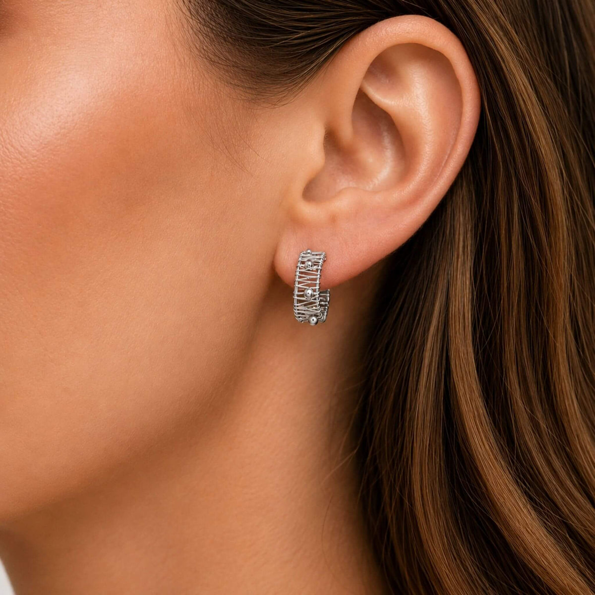 Small silver hoop earring worn on ear showing wire wrapped C-hoop design and polished bead details