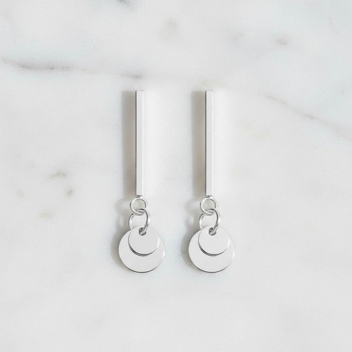 925 sterling silver bar and circle disc drop earrings flat lay on marble surface, both earrings showing full 26mm length, polished silver finish