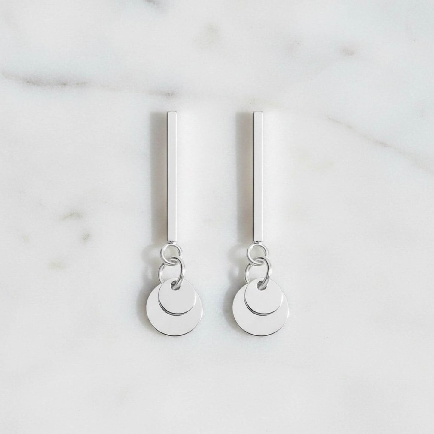 925 sterling silver bar and circle disc drop earrings flat lay on marble surface, both earrings showing full 26mm length, polished silver finish