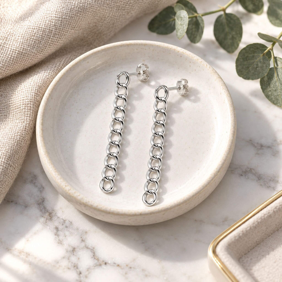Sterling silver drop earrings with polished curb chain links styled in a jewelry dish