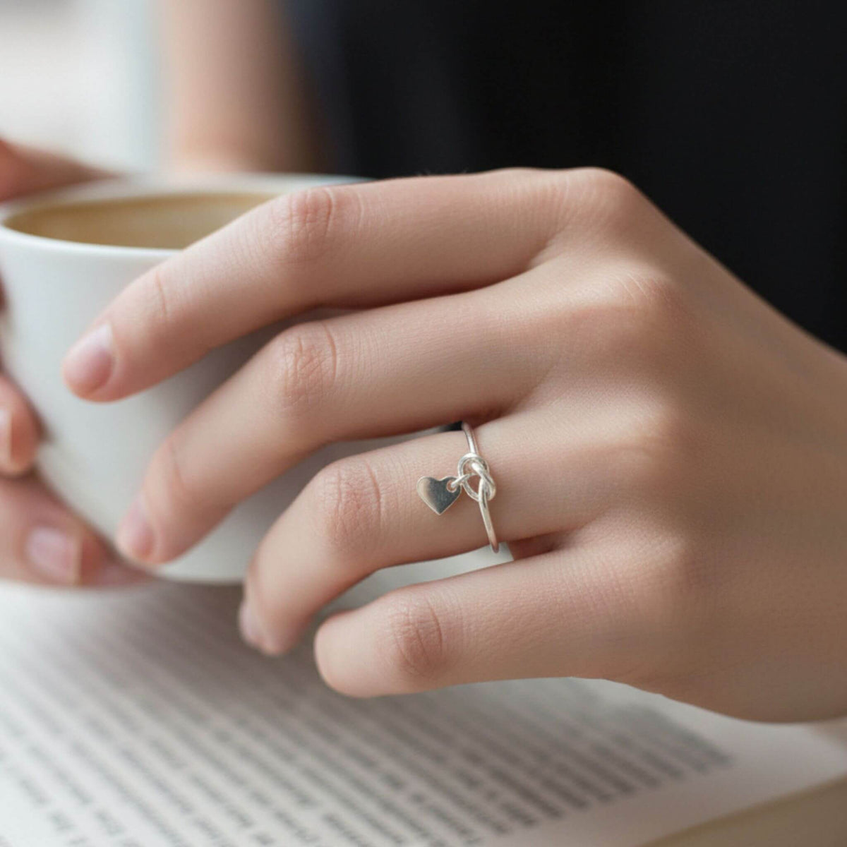 Dainty sterling silver heart love knot ring worn on hand in natural light
