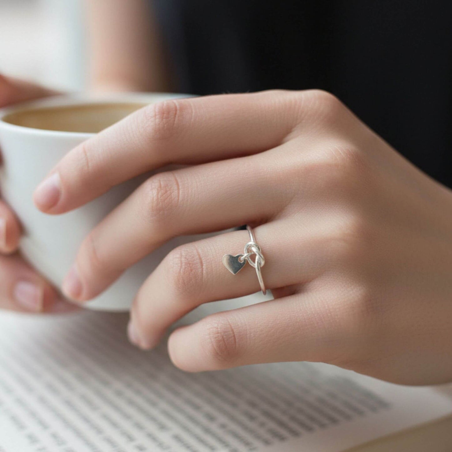 Dainty sterling silver heart love knot ring worn on hand in natural light