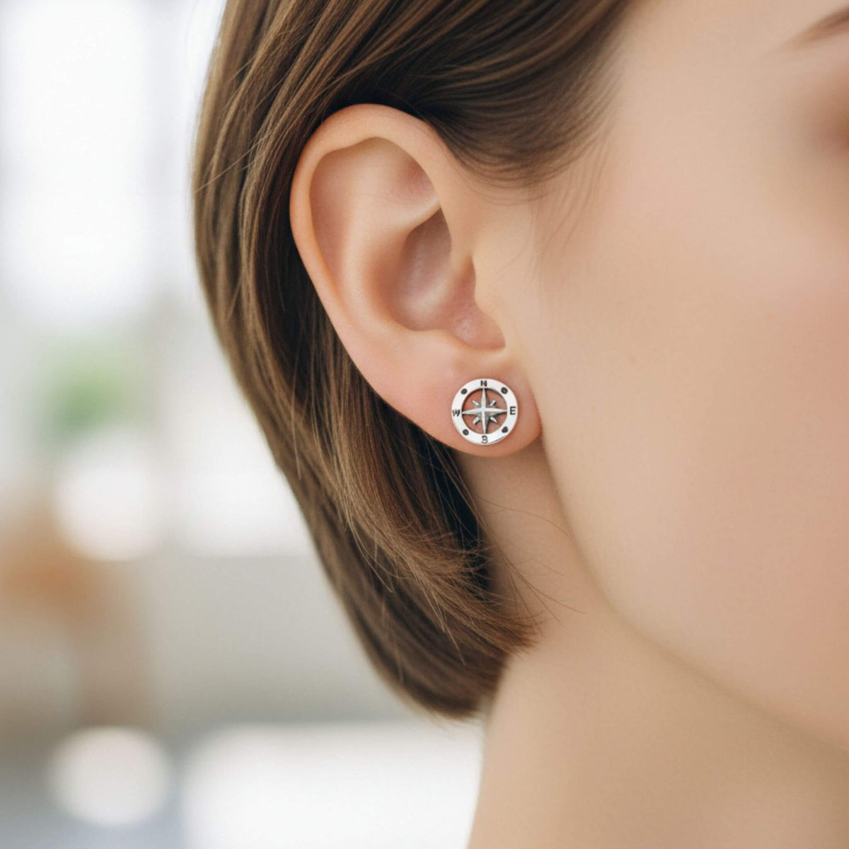 Close-up of sterling silver nautical compass stud earrings on ear