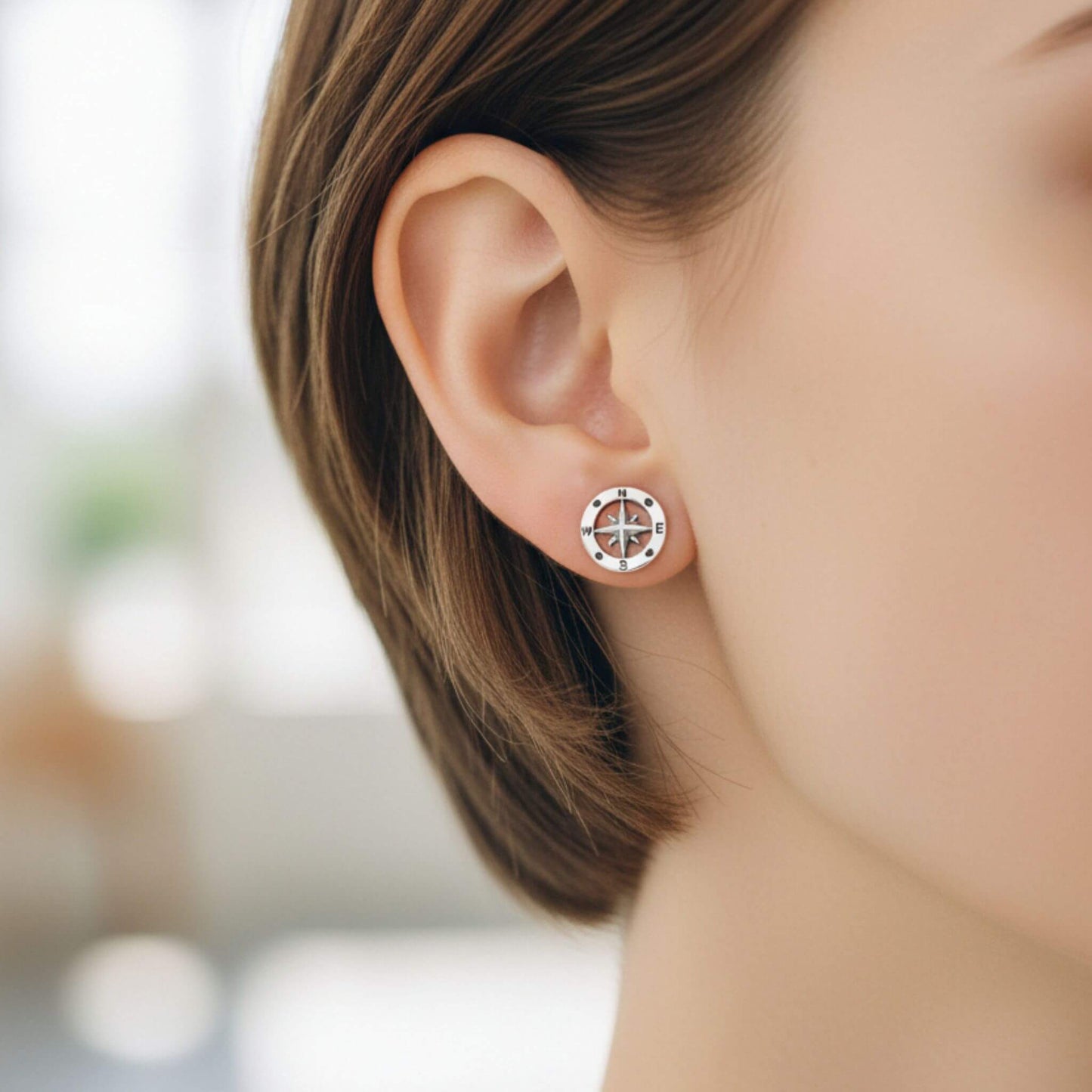 Close-up of sterling silver nautical compass stud earrings on ear