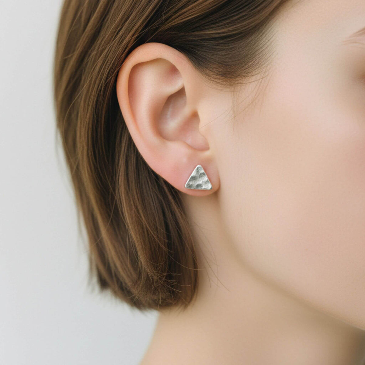 Sterling silver hammered triangle stud earrings worn on ear