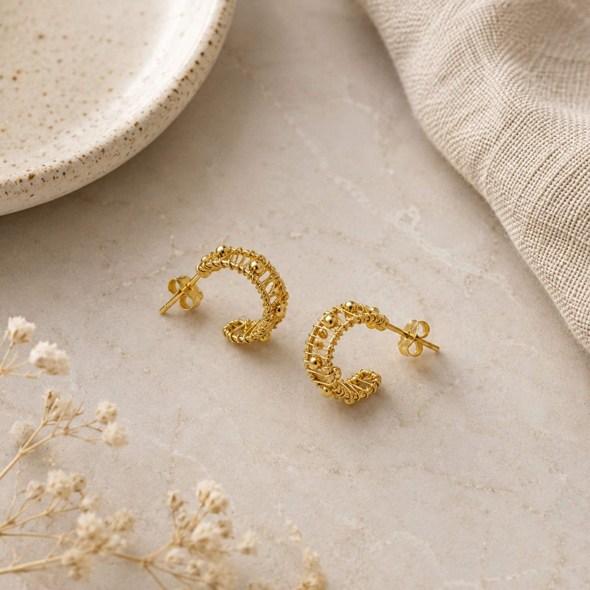 Wire wrapped gold hoop earrings with polished bead accents arranged on a neutral surface